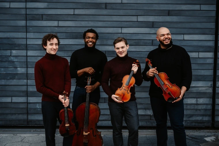 The Isidore String Quartet with their instruments. A portrait, shown for Newport Classical Music Festival in the season calendar of The Mansa Court