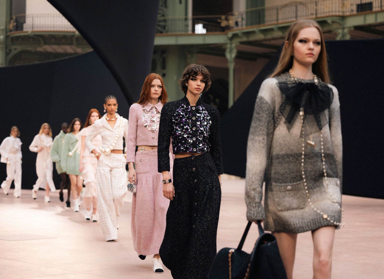 A long line of models in tweed, pearls and sequins walking in single file under the iron galleries of the Grand Palais at Paris Fashion Week