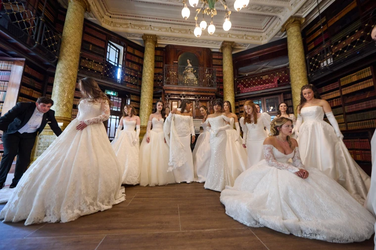Debutantes in white gowns gather in a columned library lined with books before the procession. Queen Charlotte’s Ball, One Whitehall Place, London, 2025, in the season calendar of The Mansa Court