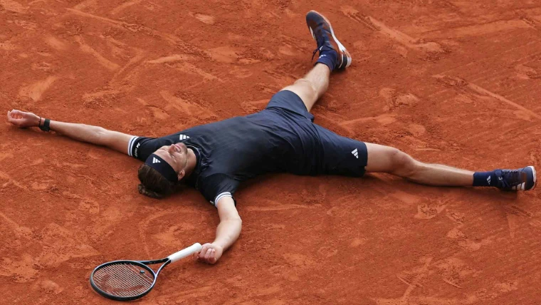 The champion lies spread-eagled on the red clay at match point, his racket beside him. The Roland Garros finals on Court Philippe-Chatrier, Paris, in the season calendar of The Mansa Court