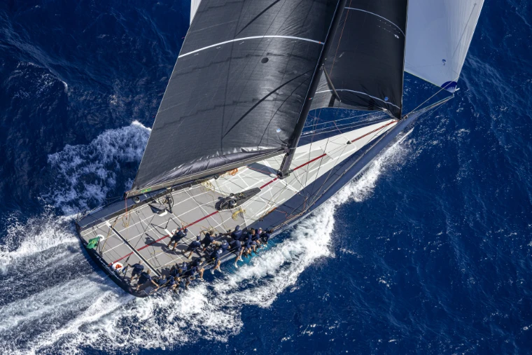 A maxi yacht from above, heeled hard with its crew on the rail, at the Maxi Yacht Rolex Cup (2026).