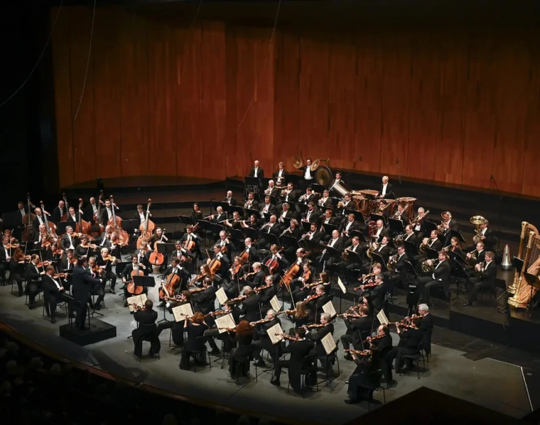 An orchestra fills the stage of the Großes Festspielhaus beneath its timber wall. Großes Festspielhaus, Salzburg (2022), shown for Salzburg Easter Festival in the season calendar of The Mansa Court