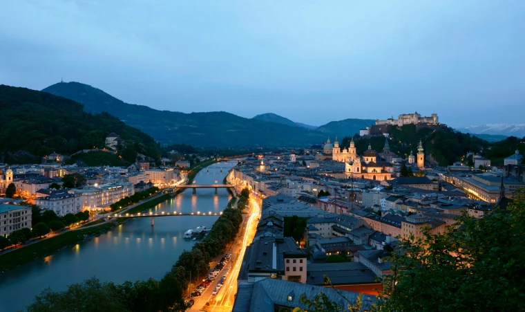 Salzburg at dusk in spring, the Salzach and the old town’s domes below the Hohensalzburg fortress. Salzburg from the Mönchsberg, shown for Salzburg Easter Festival in the season calendar of The Mansa Court
