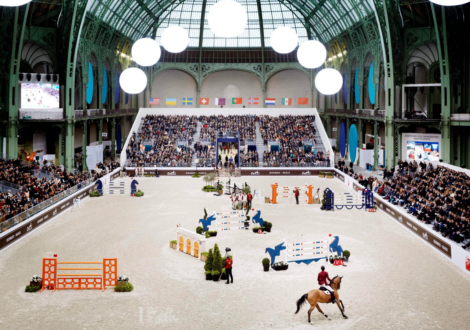 The jumping course laid out on the sand and the full grandstand seen from above at Saut Hermès, Grand Palais, Paris