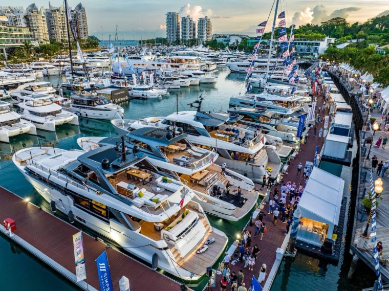 Motor yachts berthed along the crowded show pontoons at dusk, flags strung from their masts, at the Singapore Yachting Festival, a late-April engagement in the season calendar of The Mansa Court