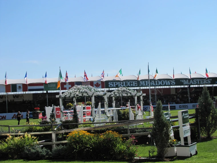 The grass International Ring with white jumps and flower beds before a grandstand hung with national flags and a Spruce Meadows ‘Masters’ banner (2011).