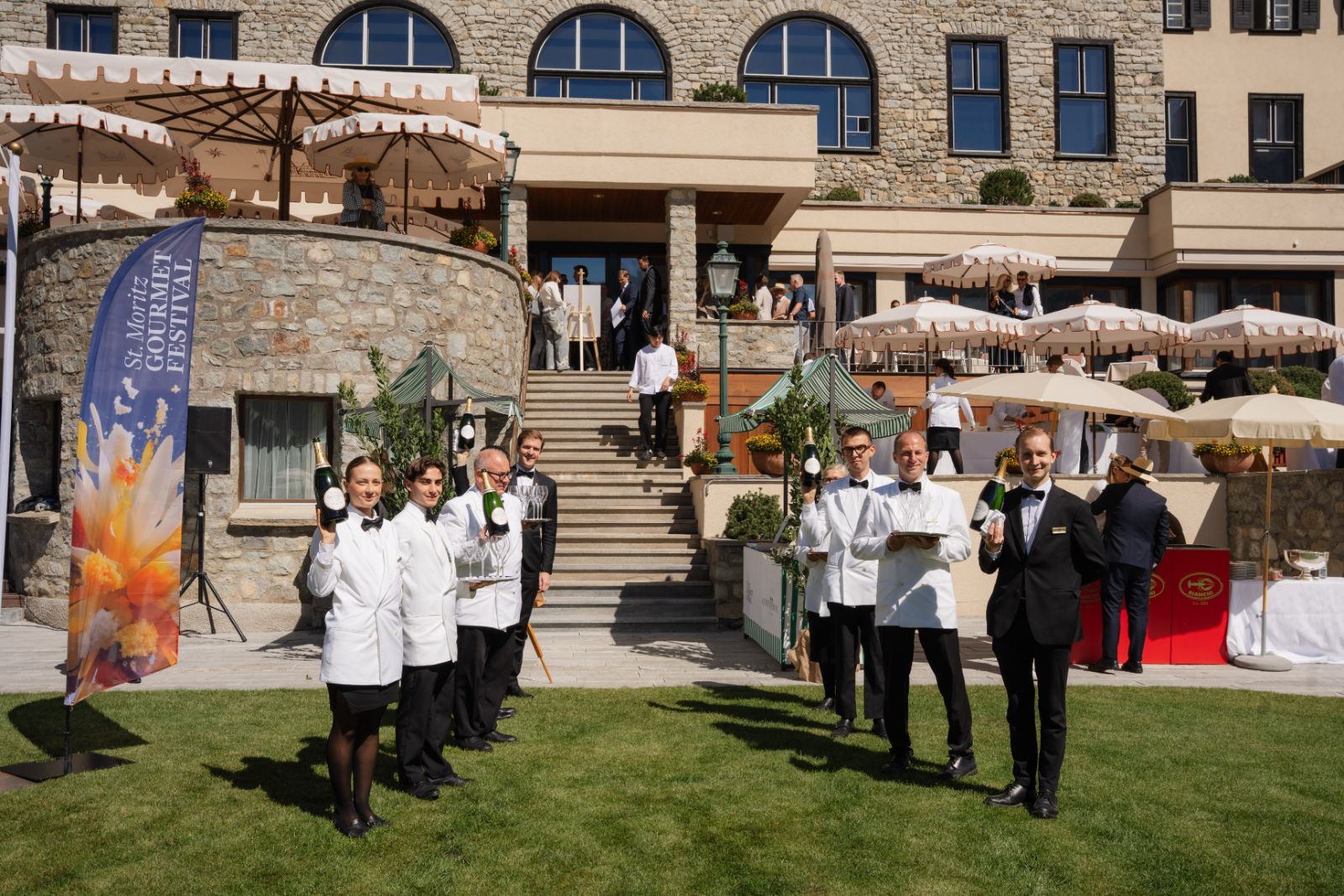 Sommeliers and waiters lined up on the lawn with champagne and glasses before the hotel steps at the St. Moritz Gourmet Festival