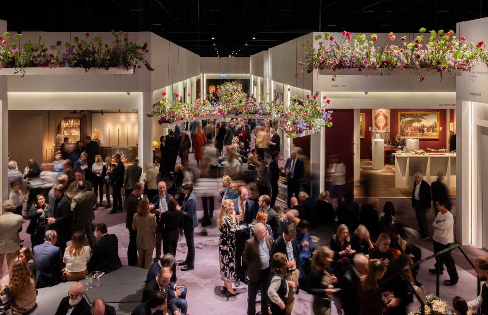Collectors and dealers on the main floor of TEFAF Maastricht beneath suspended tulip installations, the vetted art and antiques fair The Mansa Court attends each March