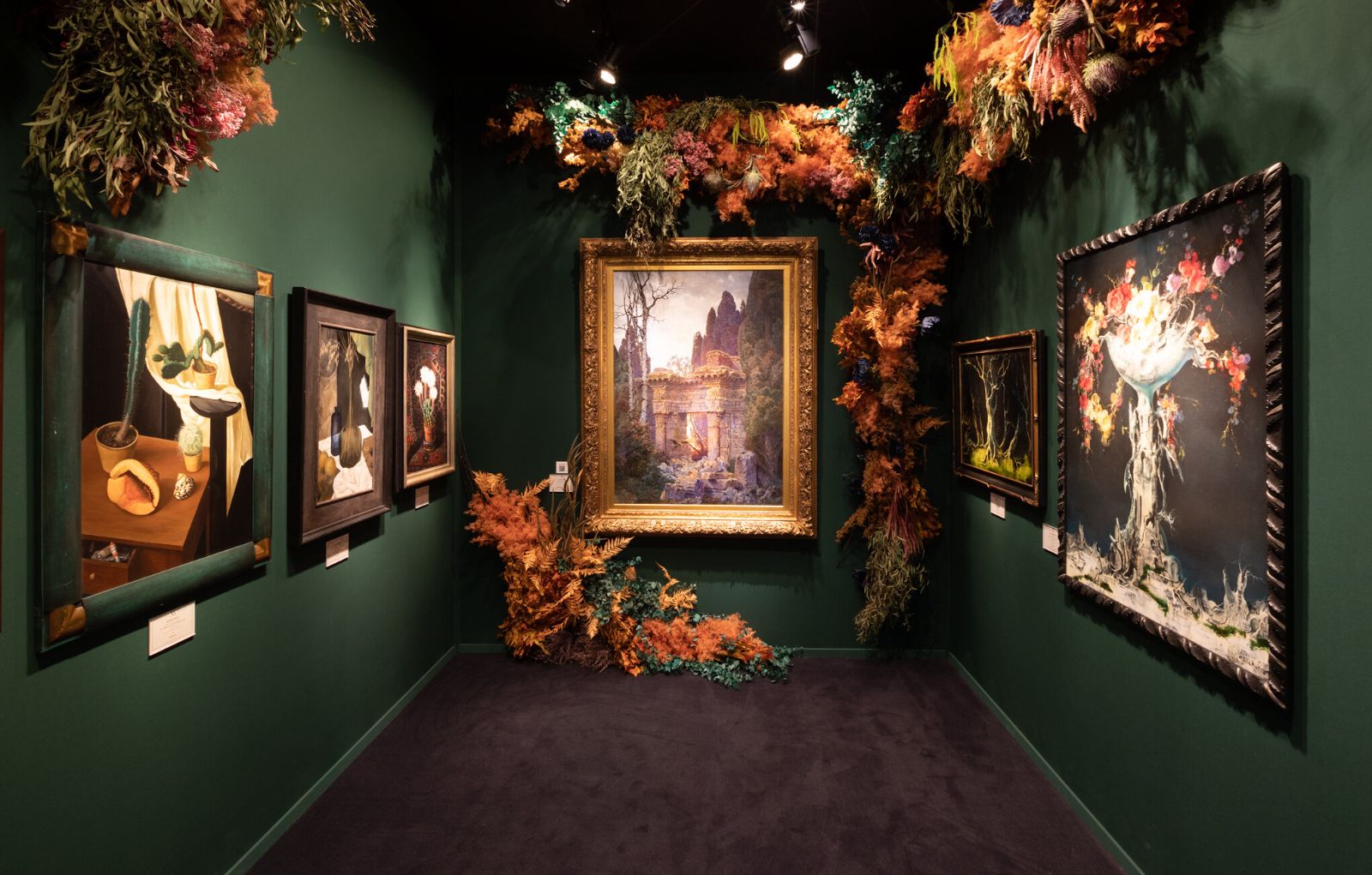 A green-walled dealer stand hung with paintings and dried flower installations at TEFAF Maastricht, attended by members of The Mansa Court
