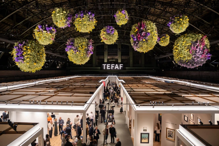 Great spheres of flowers hang above the lit stands and busy aisles of the fair in the Wade Thompson Drill Hall. TEFAF New York at the Park Avenue Armory, in the season calendar of The Mansa Court