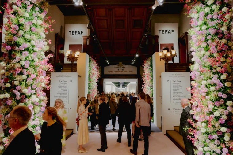 Guests gather beneath columns of pink and white flowers at the entrance to the Drill Hall. TEFAF New York at the Park Avenue Armory, in the season calendar of The Mansa Court