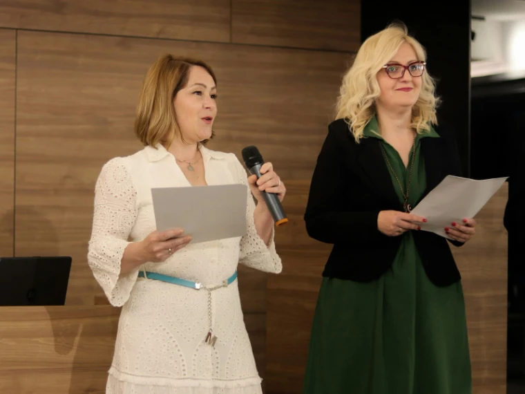 Two hosts reading from their notes, one at the microphone, in a wood-panelled room at The Acquisition in New York, hosted by The Mansa Court each April