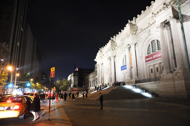 The Met’s floodlit Fifth Avenue facade and steps at night, with a few figures on the steps and a taxi on the avenue (2011).
