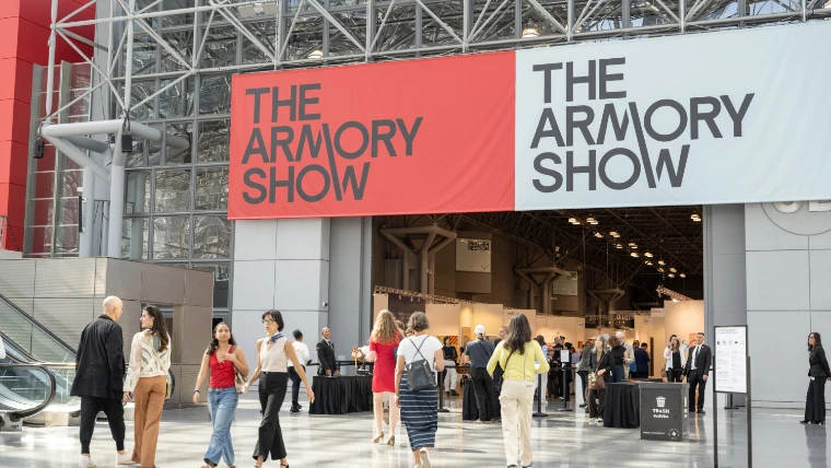 Visitors walk into the glass and steel lobby of the Javits Center beneath large red and white banners reading The Armory Show (2025).