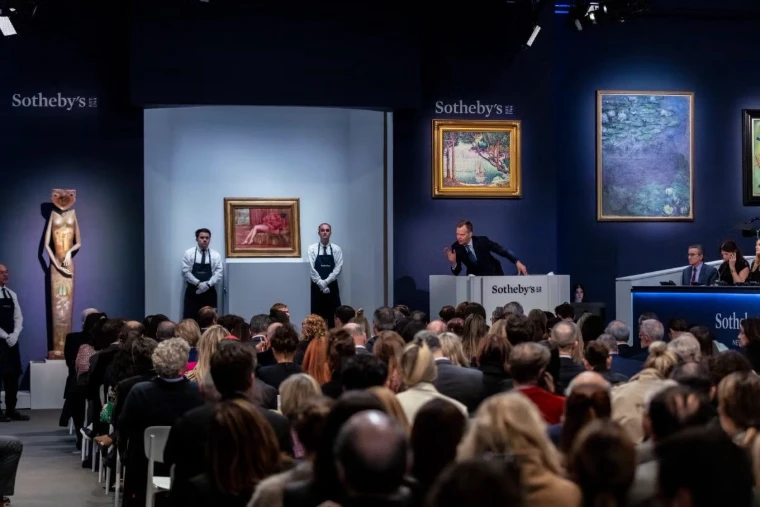 An auctioneer at the rostrum before a full saleroom and paintings on blue walls, at The Auction House Previews in New York, an engagement in the season calendar of The Mansa Court