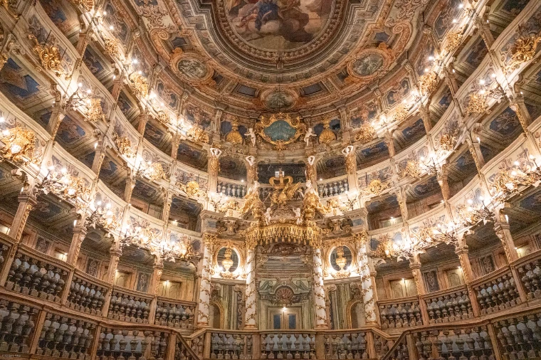 The gilded Baroque auditorium of the Margravial Opera House, its tiers of carved wooden boxes lit by candle-style lamps beneath a painted ceiling (2022).