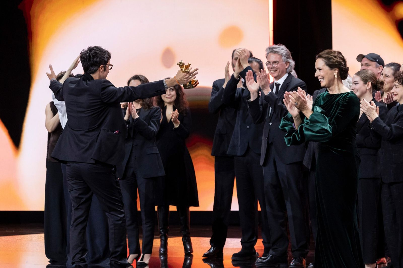 A director holding up the Golden Bear on stage as the jury and cast applaud at the award ceremony of The Berlinale