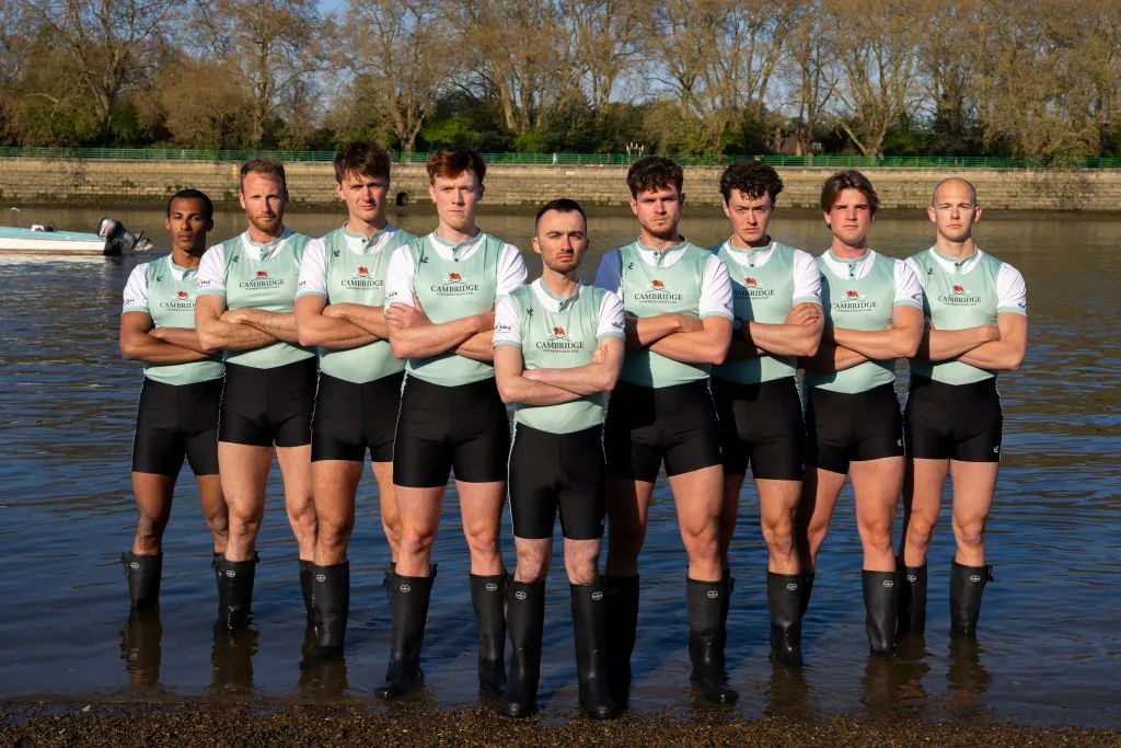 The Blue Boat crew photographed in the shallows of the Thames before The Boat Race, London, attended by members of The Mansa Court