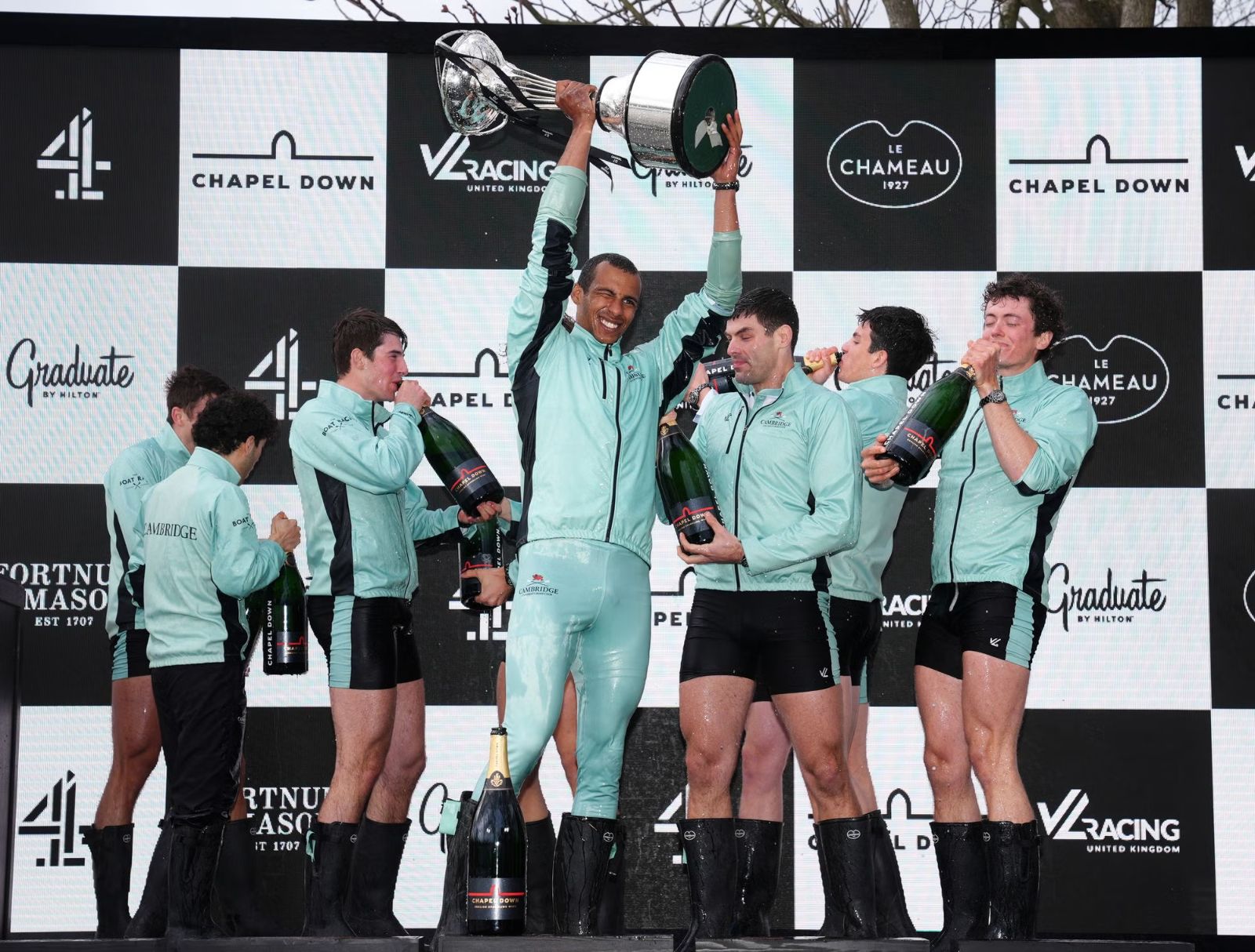 The winning crew lifting the trophy and drinking champagne after The Boat Race on the Tideway, London