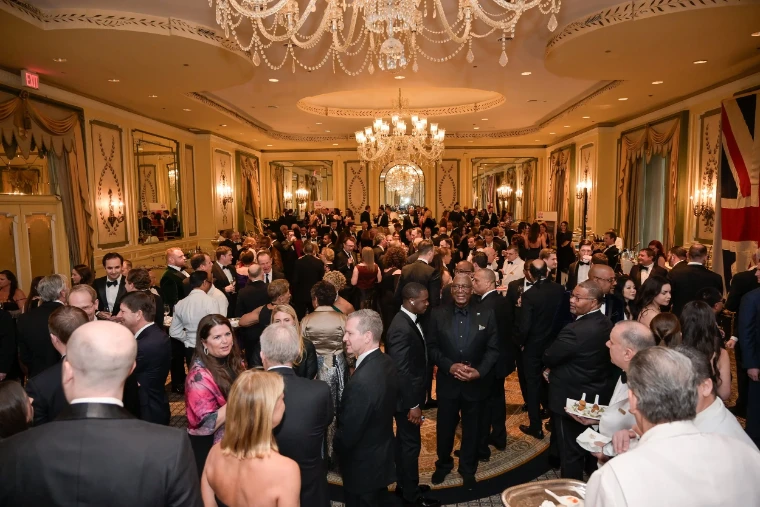 Guests in black tie at the reception of The British Ball in New York, beneath crystal chandeliers with the Union flag hung at the side of the room, an April engagement in the season calendar of The Mansa Court