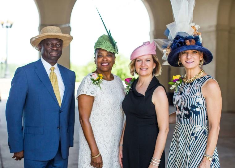 Four guests in a straw boater, a feathered green cloche, a pink pillbox and a tall navy hat pose beneath stone arches. The Central Park Conservancy Hat Luncheon in the Conservatory Garden, New York, in the season calendar of The Mansa Court