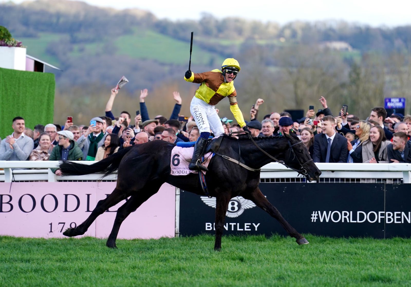 A winning jockey standing in the irons before the rail after the Gold Cup at The Cheltenham Festival, Gloucestershire, attended by members of The Mansa Court