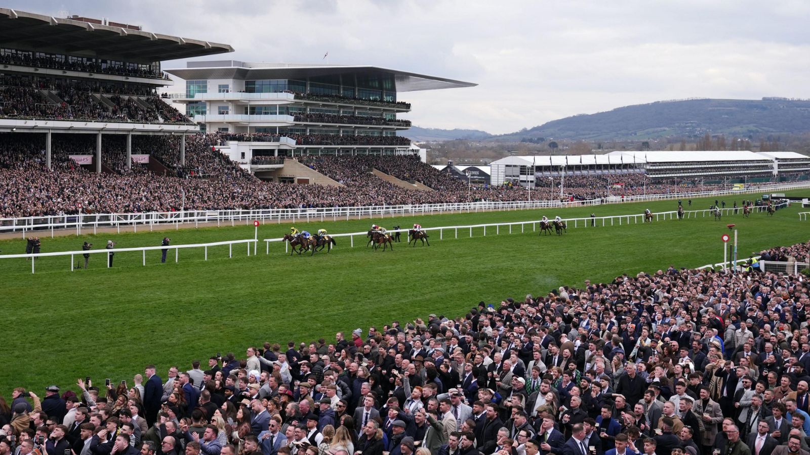 The grandstand and the crowd on the rail beneath Cleeve Hill during a race at The Cheltenham Festival, the March meeting kept in The Mansa Court calendar