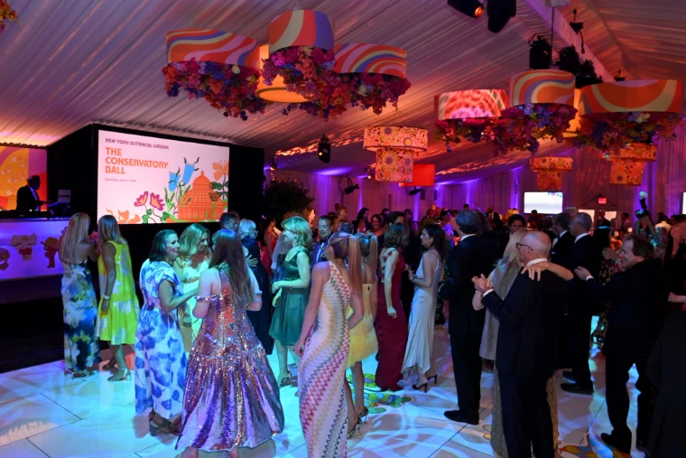 Guests in black tie and summer dresses on the dance floor beneath lampshades of flowers (2026). The Conservatory Ball at the New York Botanical Garden, the Bronx, in the season calendar of The Mansa Court