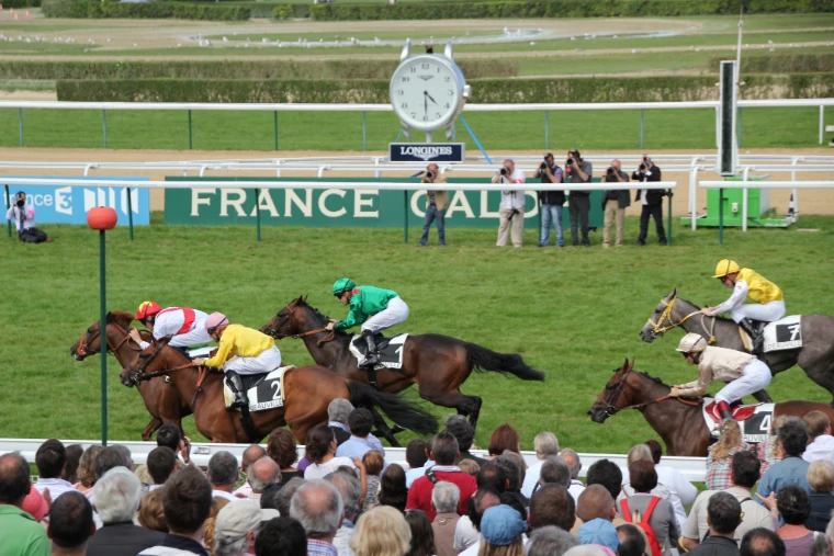 Jockeys in bright silks race past a packed rail of spectators and photographers in front of the France Galop board and Longines clock at Deauville racecourse (2011).