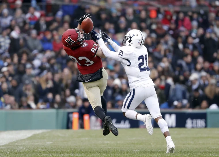 A Harvard receiver leaps for the ball over a Yale defender before a packed crowd. The Game, Harvard v Yale, Fenway Park, Boston (2018), in the season calendar of The Mansa Court