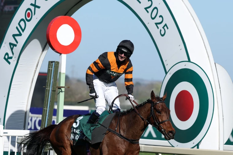 A jockey standing in the irons in celebration beneath the winning-post arch at Aintree after the 2025 Grand National, an April engagement in the season calendar of The Mansa Court