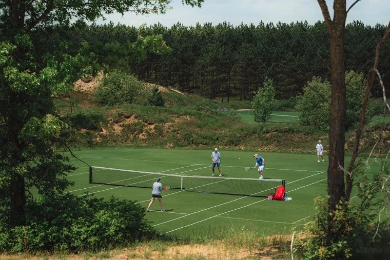 Players at doubles on a grass court cut into the woods, for The Grass Court Tennis Tournament in Southampton, New York, an afternoon in the season calendar of The Mansa Court