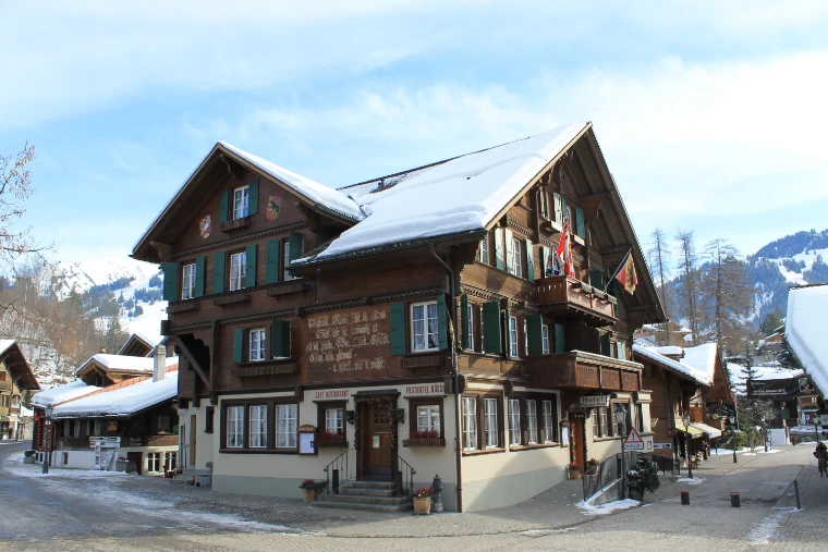 A large chalet-style hotel with green shutters and painted inscriptions on the Promenade, its roof deep in snow under a blue sky (2013).