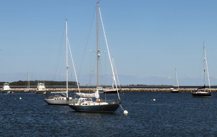 Sailing yachts lie at their moorings on blue water inside the stone breakwater under a clear sky (2016). Sag Harbor, Long Island, New York, shown for The Harbour Lunch in the season calendar of The Mansa Court