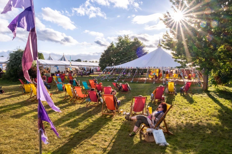 Readers in coloured deckchairs on the lawn beside the round marquee in evening sun. The Hay Festival at Hay-on-Wye, on the Welsh border, in the season calendar of The Mansa Court