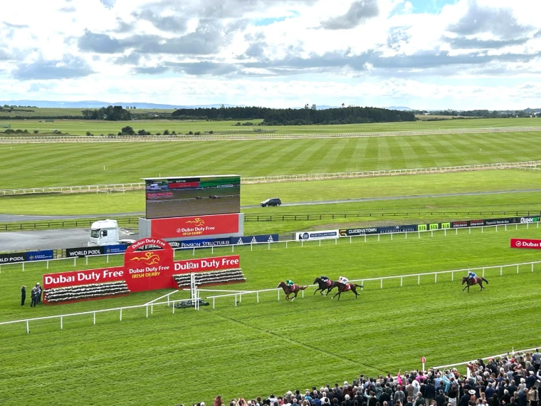 The field racing to the winning post across the open Curragh plains before the crowd in the stands at the Irish Derby, a late-June engagement in the season calendar of The Mansa Court