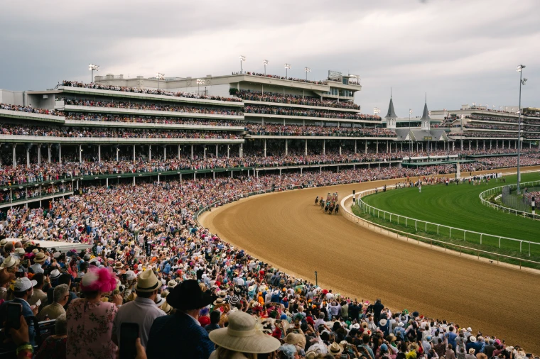 The field sweeps into the first turn before the packed grandstands and the Twin Spires. The Kentucky Derby at Churchill Downs, Louisville, in the season calendar of The Mansa Court