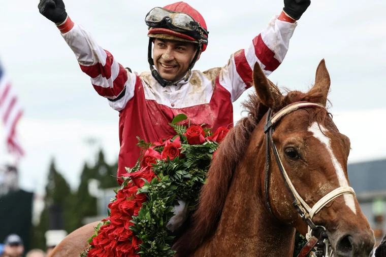 The winning jockey raises both arms astride his chestnut, draped in the garland of red roses, in 2022. The Kentucky Derby at Churchill Downs, Louisville, in the season calendar of The Mansa Court