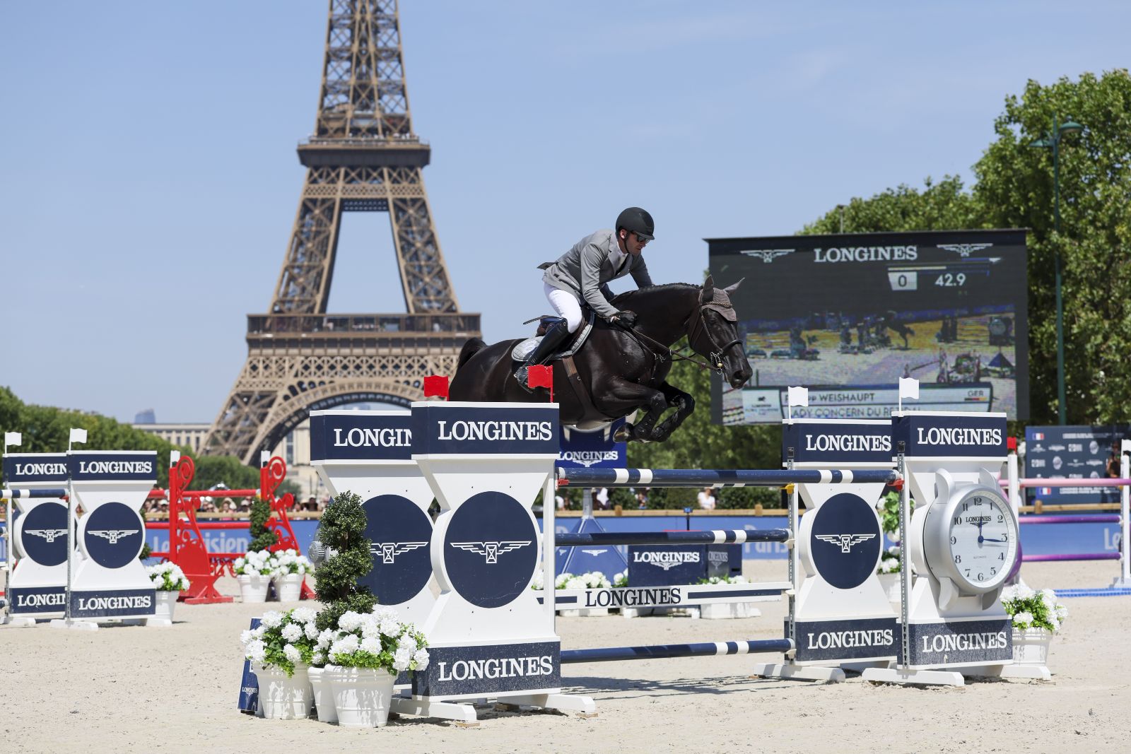 A horse and rider over a Longines fence beside the tour clock with the Eiffel Tower behind at the Longines Global Champions Tour in Paris, an engagement in The Mansa Court season calendar