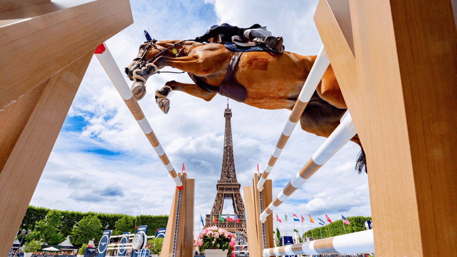 A horse and rider seen from beneath the fence with the Eiffel Tower framed between the standards at the Longines Global Champions Tour, Paris