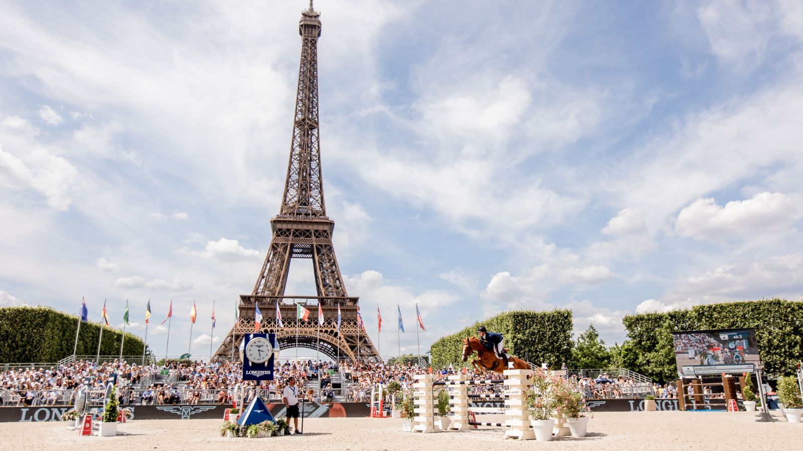 A dark horse and rider clearing the Longines oxer in the Paris arena at the Longines Global Champions Tour, attended by members of The Mansa Court