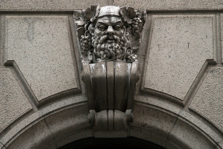 A bearded stone head crowned with grapes and vine leaves, carved as the keystone of an arch on the University Club (2008).