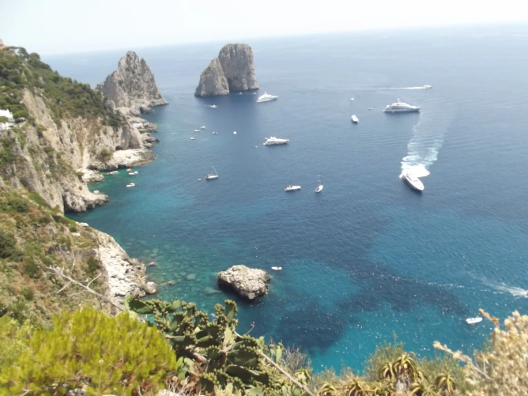 Seen from a clifftop, the Faraglioni rock stacks rise from blue sea scattered with white yachts and motorboats beside Capri’s green-and-white cliffs (2012).