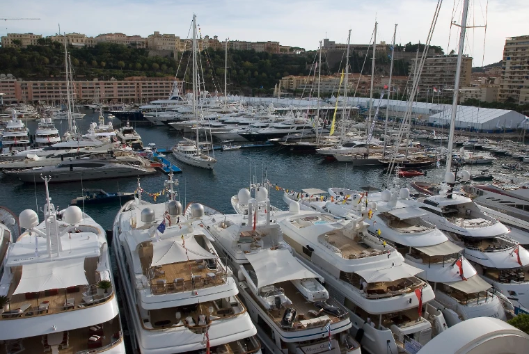 Superyachts and sailing yachts dressed with flags fill the quays of Port Hercule during the Monaco Yacht Show, with white show marquees and the Rock of Monaco behind (2011).