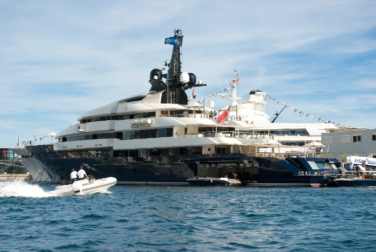 A large dark-hulled superyacht dressed with signal flags lies in Port Hercule as a white tender speeds past in the foreground (2011).