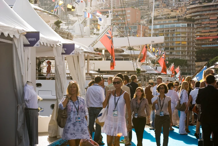 Visitors with show passes on lanyards walk along the blue-carpeted quay between white marquees and moored yachts at the Monaco Yacht Show (2011).