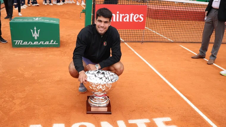 Carlos Alcaraz crouching beside the Coupe de S.A.S. le Prince Souverain on the clay after winning the 2025 Rolex Monte-Carlo Masters, an April engagement in the season calendar of The Mansa Court