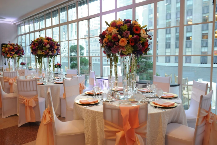 Dinner tables dressed with tall arrangements of autumn flowers beside a wall of windows at the 3 West Club.