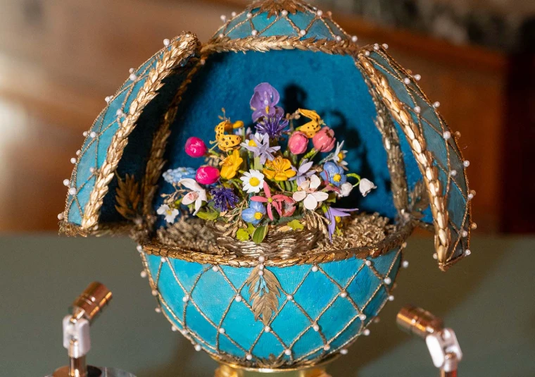 A botanical-arts entry: an egg in blue and gold, opened to a posy of flowers. The Newport Flower Show at Rosecliff, Newport, in the season calendar of The Mansa Court