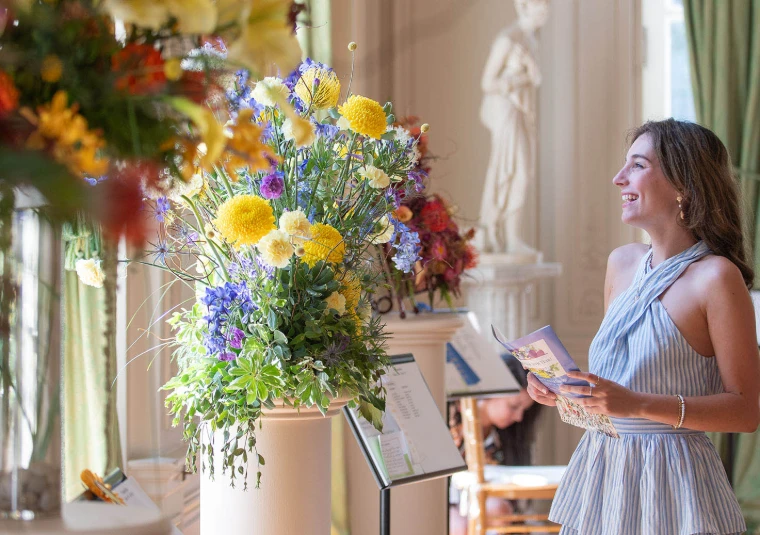 A visitor stops at an arrangement of summer flowers inside Rosecliff. The Newport Flower Show at Rosecliff, Newport, in the season calendar of The Mansa Court
